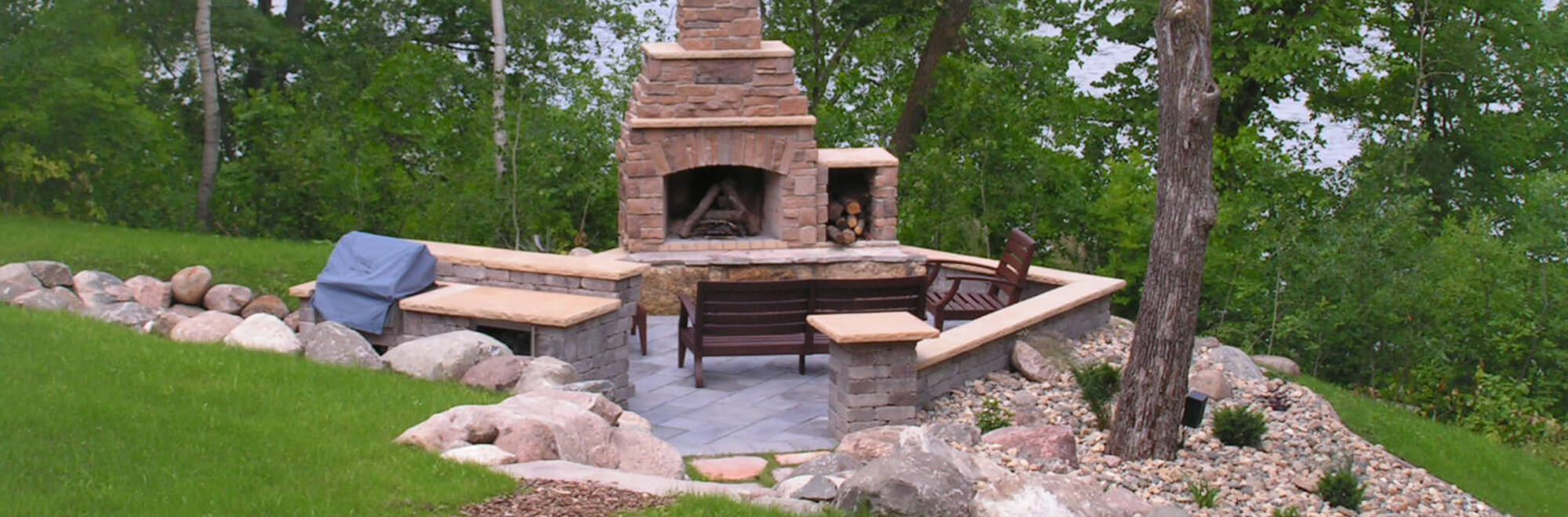 Outdoor living space in a backyard complete with paver patio, block seating wall, outdoor kitchen, and stone fireplace